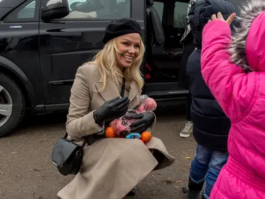 Aktris asal Kanada, Pamela Anderson memberikan buah-buahan kepada seorang anak di pengungsian Grande-Synthe, Prancis (25/1). Dalam kunjungannya, Pamela menyumbangkan buku anak-anak, makanan serta perlengkapan lainnya. (AFP/Philippe Huguen)