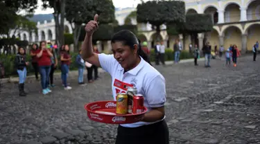 Seorang pramusaji mengacungkan jempol saat mengikuti Waiters Race ke-16 di Antigua, barat daya Ibu Kota Guatemala City, Rabu (14/11). Peserta diminta unjuk kebolehan menggunakan satu tangan membawa nampan berisi minuman. (JOHAN ORDONEZ/AFP)
