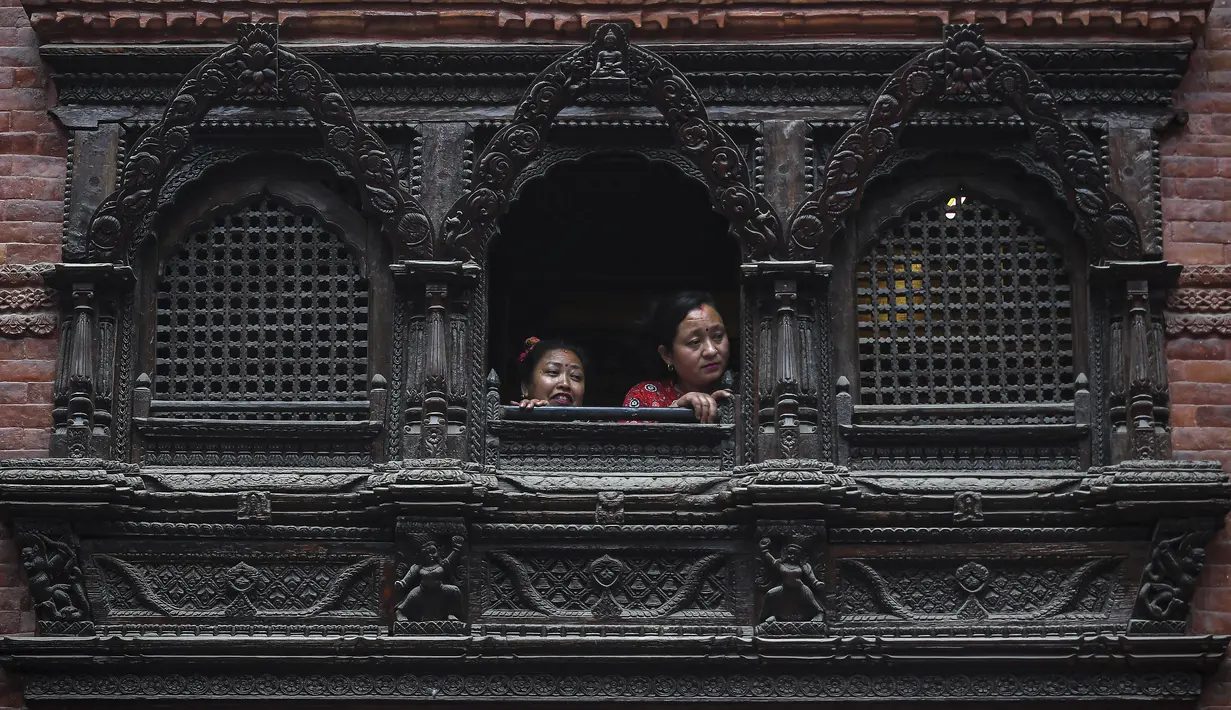 Orang-orang menonton dari jendela saat umat mengambil bagian dalam prosesi saat para imam membawa Seto Machindranath, dewa pelindung Nepal, selama festival kereta di Kathmandu (9/4/2022). (AFP/Prakash Mathema)