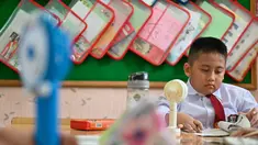 Seorang siswa sekolah dasar menggunakan kipas angin portabel untuk menyejukkan ruangan kelas saat cuaca panas di Banda Aceh pada 15 Mei 2023. (AFP/CHAIDEER MAHYUDDIN)