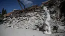 Gambar ini memperlihatkan sebuah patung di antara puing-puing bangunan yang runtuh di Hatay pada 6 Maret 2023, satu bulan setelah gempa besar melanda Turki tenggara. Pejabat Turki mengatakan 214.000 bangunan hancur setelah gempa, banyak di antaranya di Hatay dan Kahramanmaras. (Photo by OZAN KOSE / AFP)