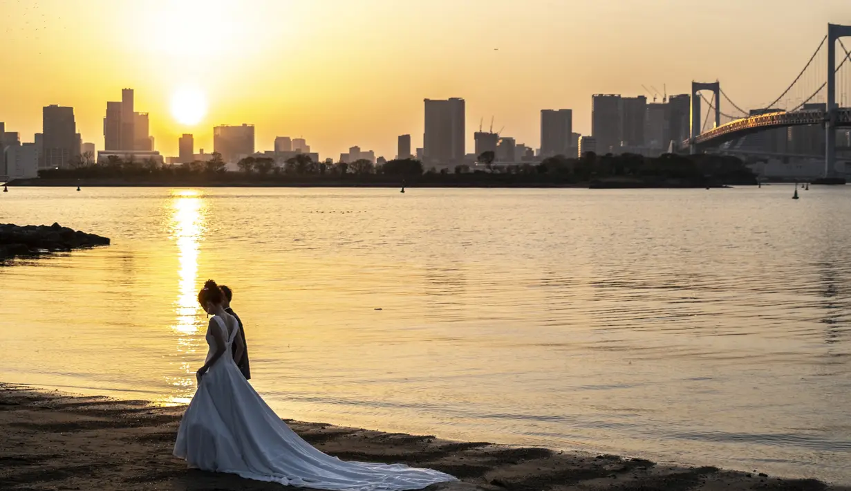 Sepasang kekasih berpose selama pemotretan pernikahan pada hari yang cerah di tepi teluk di daerah Odaiba Tokyo (12/4/2022). Para pengunjung biasanya datang ke Seaside Park untuk menikmati pemandangan Gunung Fuji dari bianglala Daikanransha. (AFP/Charly Triballeau)