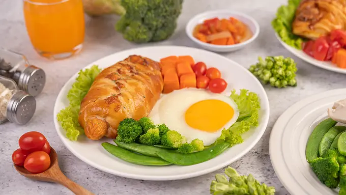 Sepiring roti, sayuran, buah, dan telur goreng serta berbagai sayuran dan segelas jus jeruk (Foto Dok: Freepik/jcomp)