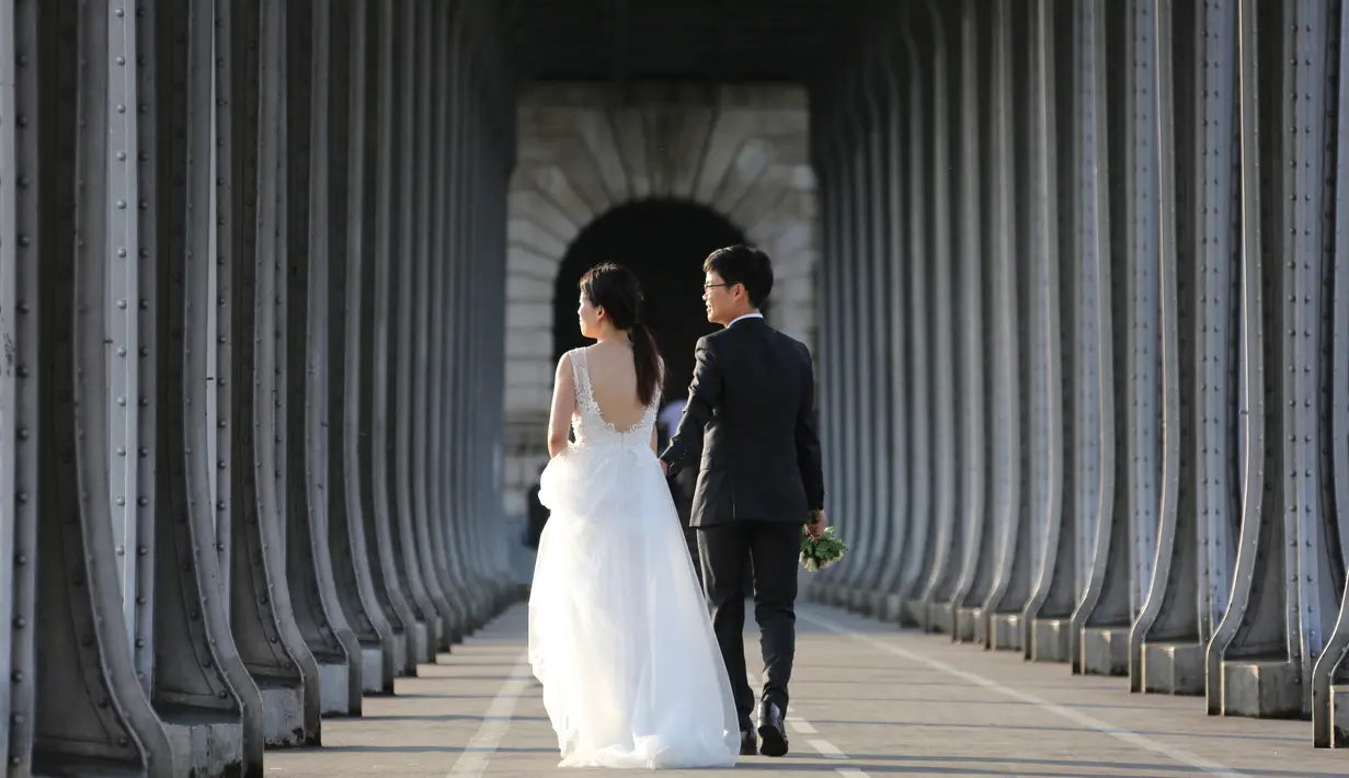 Sepasang calon pengantin asal Asia melakukan foto prewedding di bawah Jembatan Pont de Bir Hakeim, di atas permukaan sungai Seine ketika matahari terbit di Paris, 25 Juli 2017. (AFP PHOTO / LUDOVIC MARIN)