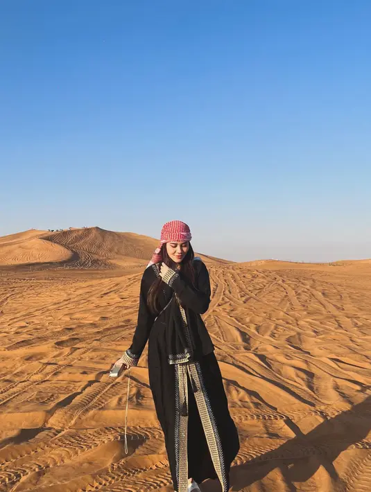 Ia kenakan gamis hitam keemasan berpayet dan sorban merah di kepala. Dilengkapi dengan sandal putih dan sling bag hitam [@aaliyah.massaid]