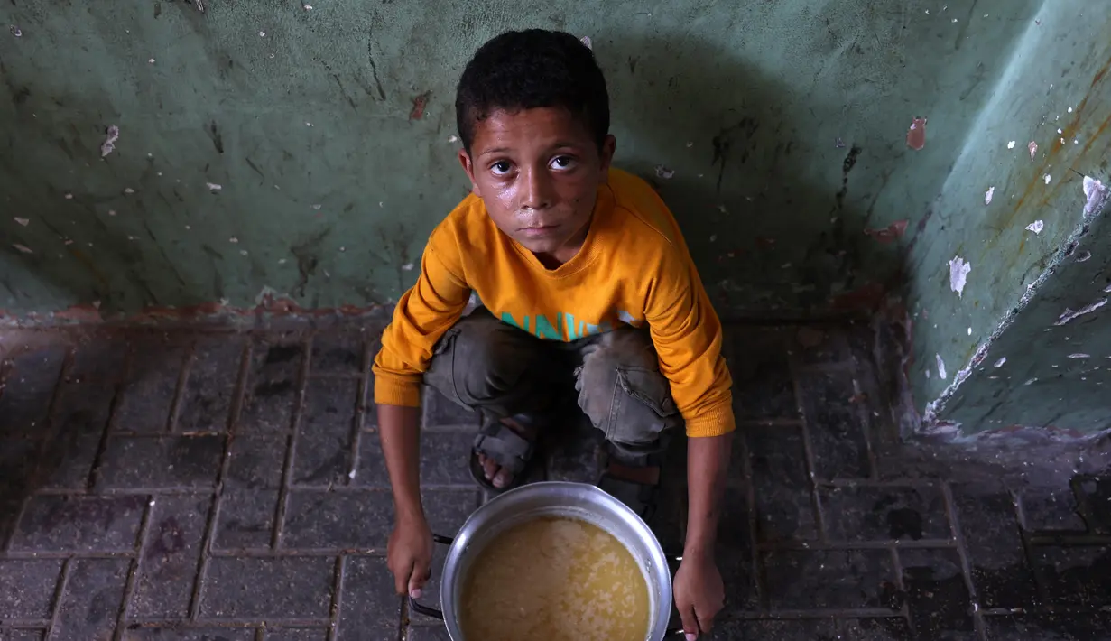 Seorang anak Palestina yang mengungsi duduk di samping sepanci sup miju-miju yang ia terima di sebuah titik distribusi makanan di Kota Gaza di Jalur Gaza utara pada 25 Juli 2025. (Omar AL-QATTAA/AFP)