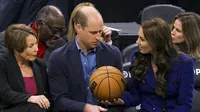 Kate Middleton, Putri Wales memberikan bola basket kepada Pangeran Inggris William disaksikan Gubernur terpilih Massachusetts Maura Healey (kiri) selama pertandingan NBA antara Boston Celtics dan Miami Heat di TD Garden di pusat kota Boston, pada 30 November 2022. (Photo by Brian Snyder/Pool/AFP)