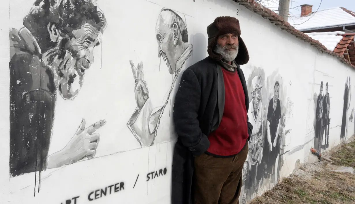 Nikolay berpose di depan mural bergambar dirinya bersama Paus Fransiskus di desa Staro Zhelezare, Bulgaria, Kamis (27/7). Penduduk setempat memenuhi dinding bagian luar rumah mereka dengan mural sejumlah tokoh dan musisi dunia (AP Photo/Valentina Petrova)