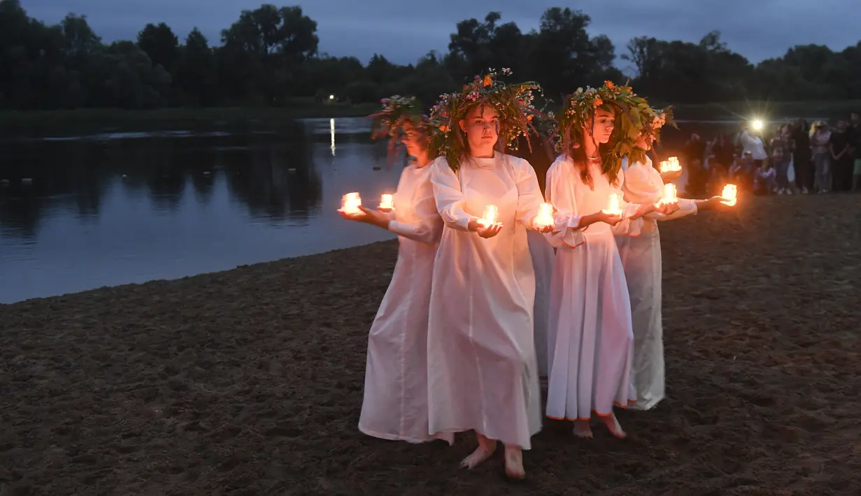 Gadis-gadis Belarusia memegang lilin saat berdiri di Sungai Berezina pada Hari Ivan Kupala di Desa Parichi, sekitar 200 km (125 mil) selatan Parichi, Belarusia, 6 Juli 2022. Hari Ivan Kupala merupakan sebuah perayaan malam kuno yang menandai Titik Balik Matahari Musim Panas, malam terpendek tahun ini. (AP Photo/Viktor Drachev)