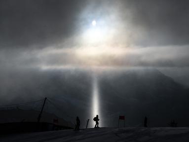 Pelatih berjalan melintasi sinar cahaya, saat melakukan pemeriksaan jalur ski dalam Kejuaraan FIS Alpine World Ski. (Foto: AFP/Fabrice Coffrini)