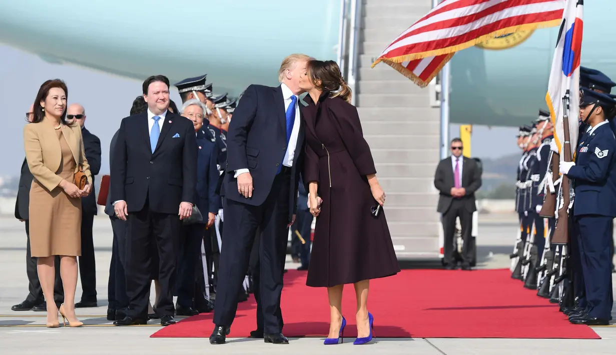 Para pejabat tinggi Korsel menyaksikan Presiden Donald Trump dan Melania berciuman di Pangkalan Udara Osan, Korea Selatan, (7/11). Trump melakukan kunjungan ke lima negara Asia Jepang, Korea Selatan, China, Vietnam dan Filipina. (AP Photo / Andrew Harnik)