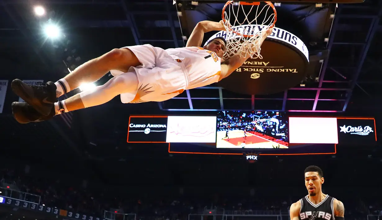 Pemain Phoenix Suns, Devin Booker bergantungan pada ring basket usai melakukan dunks saat melawan San Antonio Spurs pada laga NBA di Talking Stick Resort Arena, (15/12/2016). Spurs menang 107-92. (Reuters/Mark J. Rebilas-USA TODAY Sports)