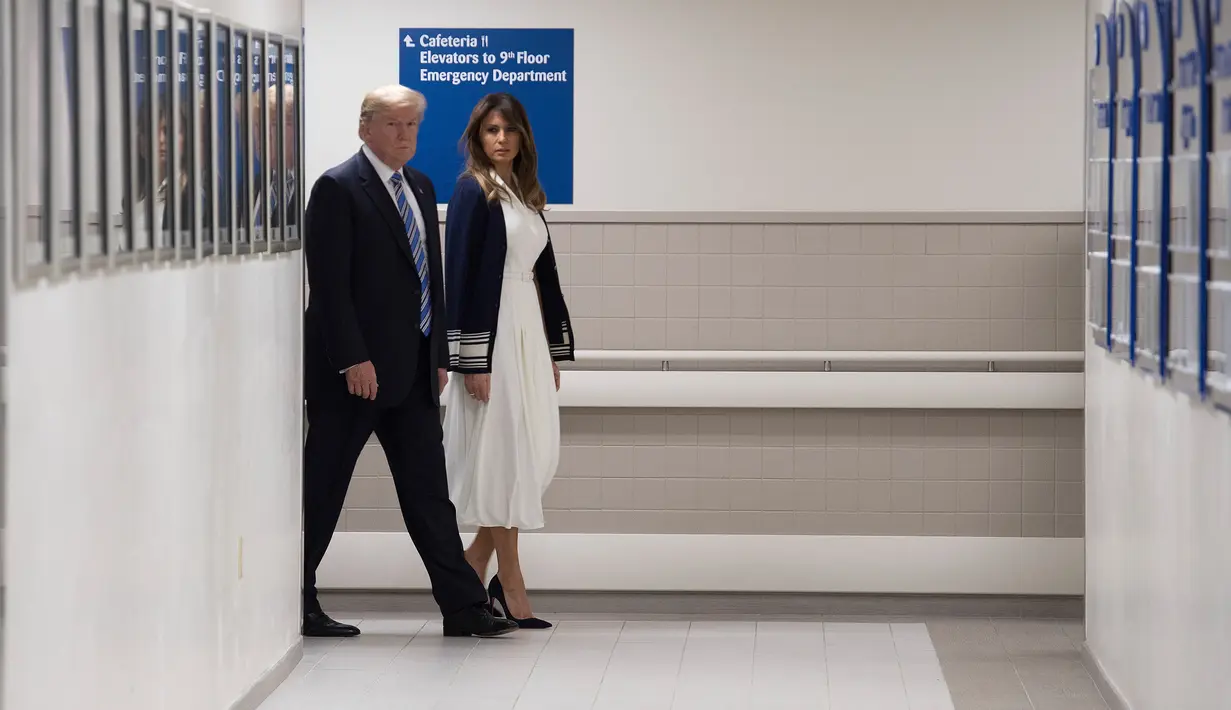 Presiden AS Donald Trump berjalan bersama istrinya di lorong rumah sakit di Florida (16/2). Trump mengunjungi rumah sakit tersebut untuk memberi penghormatan kepada korban penembakan massal yang menewaskan 17 orang. (AFP Photo/Jim Watson)