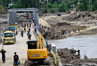 Akses utama yang menghubungkan Banda Aceh-Medan sempat lumpuh dan distribusi logistik terganggu. Tampak dalam foto, warga menyeberangi sungai di jembatan yang baru dibangun yang menghubungkan Aceh dan Provinsi Sumatera Utara setelah hancur akibat banjir bandang di Sungai Peusangan, Distrik Bireuen, Provinsi Aceh, Selasa 9 Desember 2025. (CHAIDEER MAHYUDDIN/AFP)