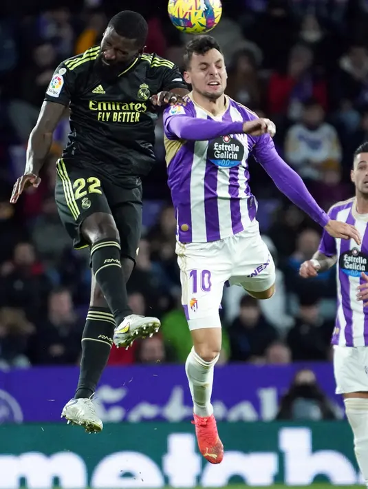 Bek Real Madrid Antonio Rudiger (Kiri) dan penyerang Real Valladolid  Oscar Plano berebut menyundul bola dalam duel pekan ke-15 La Liga 2022/23 di Stadion Nuevo Jose Zorrilla, Valladolid, Sabtu (31/12/2022) dini hari WIB.  Real Madrid harus berjuang keras untuk melewati perlawanan tangguh Real Valladolid. (CESAR MANSO / AFP)