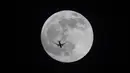 Sebuah pesawat terbang melewati bulan purnama di atas Basra, Irak, Minggu (15/5/2022). (AP Photo/Nabil al-Jurani)