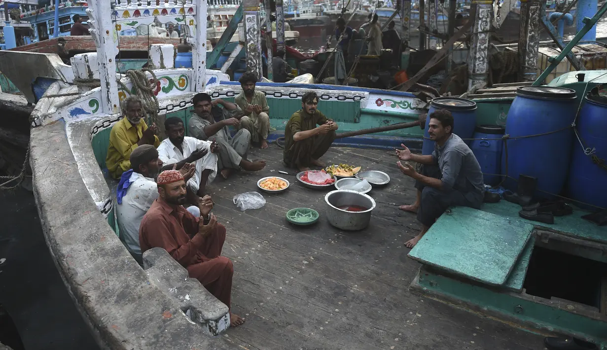 Nelayan duduk di atas kapal saat mereka berdoa sebelum berbuka puasa selama bulan suci Ramadhan di galangan kapal di kota pelabuhan Karachi, Pakistan pada 18 April 2022. Setelah menjalani ibadah puasa, waktu buka puasa menjadi momen yang dinanti oleh umat Islam. (Rizwan TABASSUM / AFP)