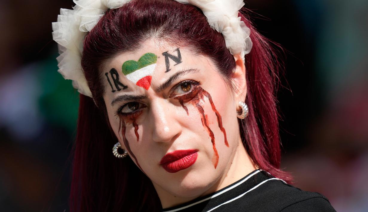 Seorang wanita berdiri di tribun dengan wajah dicat untuk mengenang Mahsa Amini, seorang wanita yang meninggal saat berada dalam tahanan polisi di Iran pada usia 22 tahun, sebelum pertandingan sepak bola Grup B Piala Dunia 2022 antara Wales dan Iran di Ahmad Bin Ali Stadium, Al Rayyan, Qatar, Jumat (25/11/2022). (AP Photo/Frank Augstein)