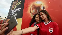Dua wanita berselfie saat acara tur dunia trofi Piala Dunia FIFA  2018 di Ibu Kota Kairo, Mesir (15/3). Trofi ini terbuat dari emas murni 18 karat dengan dasar perunggu, setinggi 36,8 sentimeter dan berat 6,1 kilogram. (AFP Photo/Khaled Desouki)