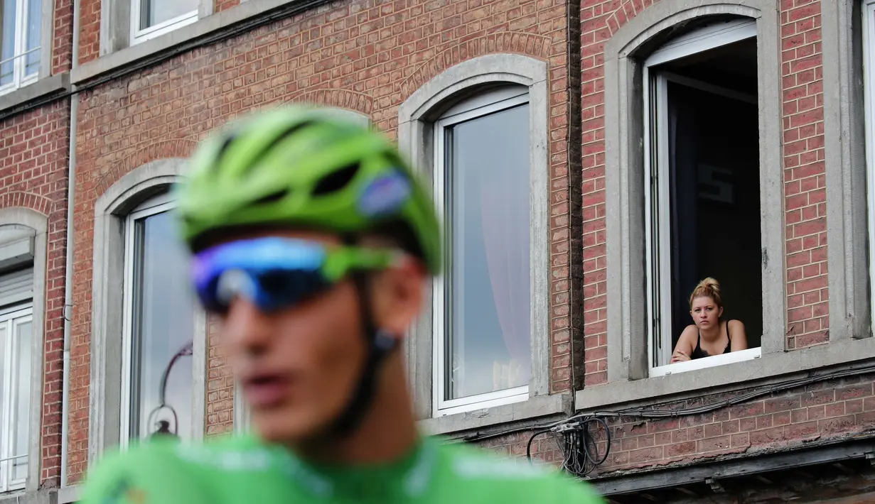 Seorang wanita menonton dari jendela saat pebalap Jerman, Marcel Kittel meraih jersey hijau pada etape ketiga Tour de France dari Verviers, Belgia dan finish di Longwy, Prancis, (3/7/2017). (AP/Christophe Ena)