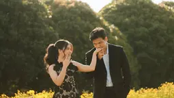 Di foto lainnya, pasangan ini memilih padang bunga kuning sebagai latar belakang. Indah memancarkan pesona feminin dalam gaun hitam dengan aksen renda floral, sementara Frans tetap tampil serasi dengan setelan formal. Momen candid ketika Frans mencium tangan Indah sambil tertawa menggambarkan kedekatan mereka yang penuh cinta di tengah suasana hangat. (Liputan6.com/IG/@fransfaisal_)