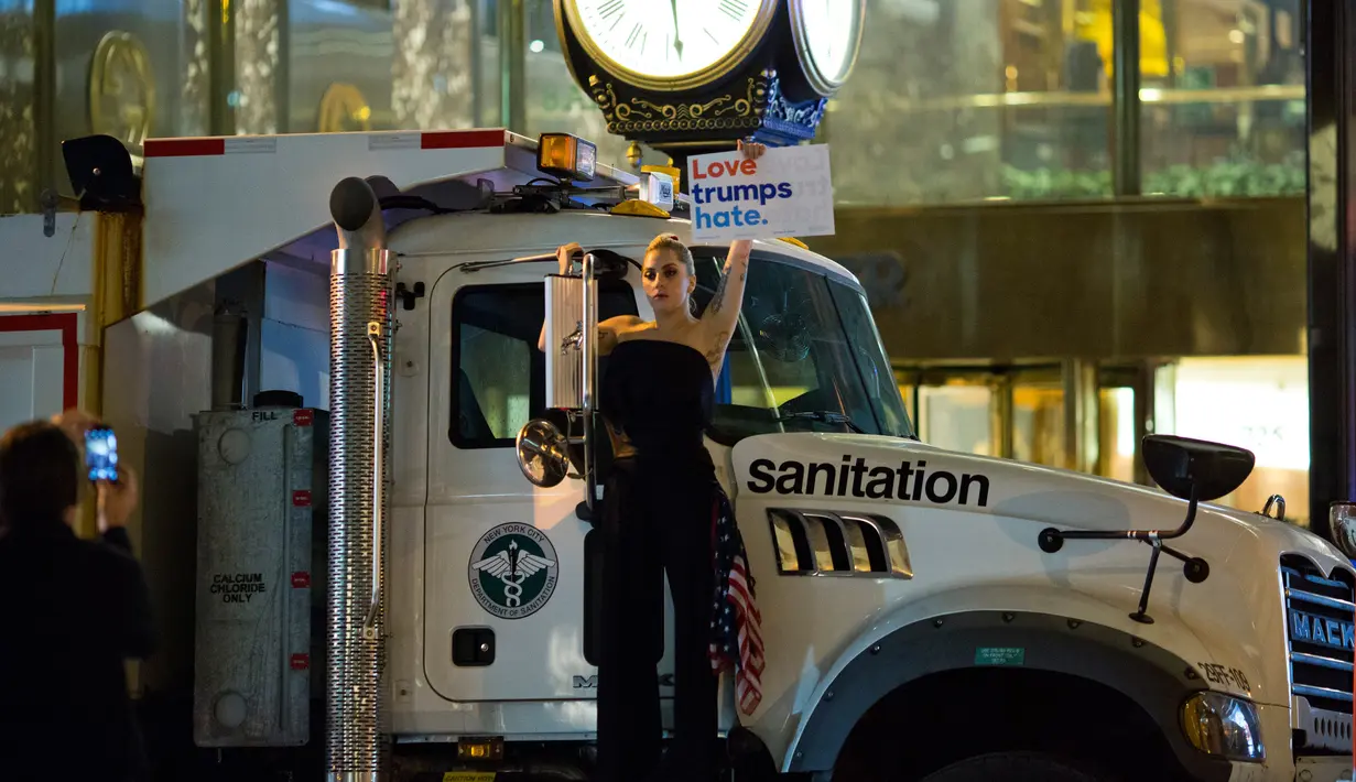 Penyanyi Lady Gaga berbusana serba hitam dan membawa bendera AS berunjuk rasa di depan Trump Tower, New York City, AS (9/11). Sebagai bentuk protesnya, Gaga mengangkat poster bertuliskan “Love Trumps Hate.”( AFP PHOTO / Dominick Reuter)