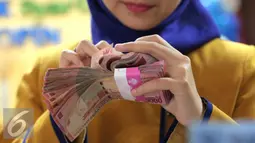 Petugas Bank menghitung uang pecahan Rp100.000 di Bank Bukopin Syariah, Jakarta, Selasa (29/12). Di pasar spot, Senin (28/12), rupiah melemah tipis 0,08% ke Rp 13.642 per dollar AS. (Liputan6.com/Angga Yuniar)