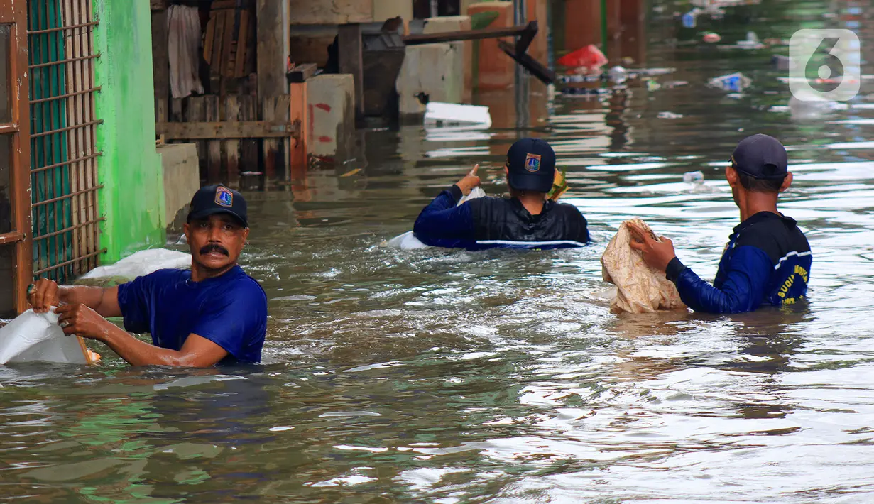 Petugas Sudin Sumber Daya Air (SDA) memunguti sampah-sampah yang tergenang saat banjir di kawasan Kampung Melayu Kecil, Bukit Duri, Jakarta, Selasa (25/2/2020). Banjir tersebut akibat luapan sungai Ciliwung. (merdeka.com/magang/ Muhammad Fayyadh)