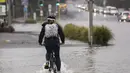 Seorang pengendara sepeda melewati banjir di Auckland, Selandia Baru, Rabu (1/2/2023). Peringatan hujan lebat untuk Auckland dicabut, meskipun keadaan darurat tetap berlaku untuk kota terbesar di negara itu setelah rekor curah hujan dan banjir pada hari Jumat menewaskan empat orang orang dan menyebabkan gangguan yang meluas. (Dean Purcell/New Zealand Herald via AP)