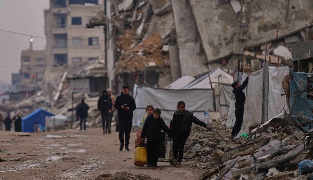 Kepala Badan Perserikatan Bangsa Bangsa (PBB) untuk Pengungsi Palestina (UNRWA), Philippe Lazzarini mengatakan selama berbulan-bulan konflik, ratusan ribu warga terpaksa tinggal di reruntuhan bangunan, tempat perlindungan darurat, serta tenda-tenda darurat yang tidak mampu melindungi dari hujan lebat dan angin kencang. Tampak dalam foto, warga Palestina berjalan di sepanjang jalan yang dikelilingi bangunan-bangunan yang hancur akibat serangan udara dan darat Israel di lingkungan Sheikh Radwan, Kota Gaza, Selasa, 30 Desember 2025. (AP Photo/Abdel Kareem Hana)