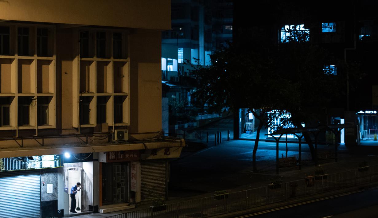 Penjaga keamanan memegang sapu pada subuh hari di pintu masuk sebuah bangunan di distrik Kwai Chung, Hong Kong (25/5/2019). Kwai Chung adalah situs pelabuhan peti kemas. Ini juga merupakan bagian dari Kota Baru Tsuen Wan. Pada tahun 2000, ia memiliki populasi 287.000. (AFP Photo/Philip Fong)