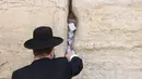 Seorang pria Yahudi ultra-Ortodoks menempatkan catatan saat dia berdoa di Tembok Barat di Kota Tua Yerusalem (30/3/2022). Pembersihan sebagai persiapan untuk liburan Paskah Yahudi yang akan datang. (AFP/Hazem Bader)
