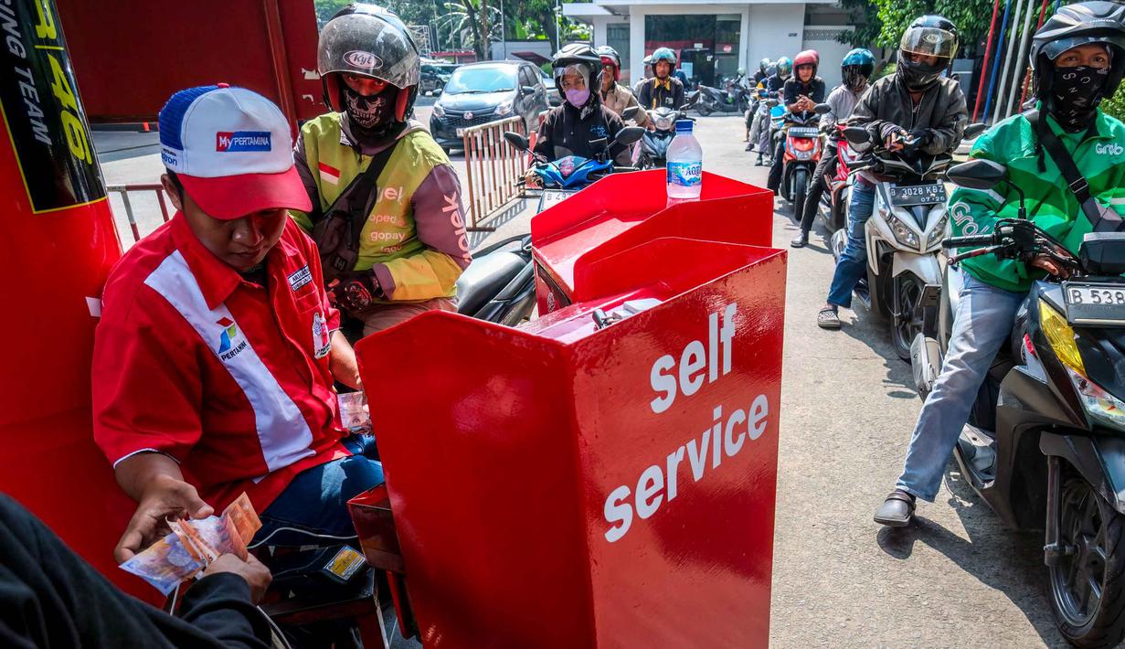 Seorang pekerja SPBU (kiri) menerima pembayaran dari pengendara yang mengantre untuk mengisi bahan bakar sepeda motor mereka di sebuah Stasiun Pengisian Bahan Bakar Umum (SPBU), Jakarta pada Rabu 1 April 2026. Pemerintah resmi tidak mengubah harga Bahan Bakar Minyak (BBM) di dalam negeri, baik harga BBM subsidi maupun non subsidi. (BAY ISMOYO/AFP)