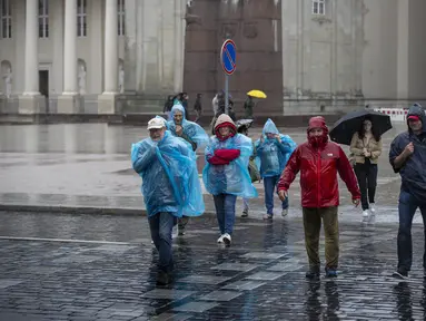 Orang-orang menyeberang jalan saat hari hujan, di Vilnius, Lituania, Senin (29/7/2024). (AP Photo/Mindaugas Kulbis)