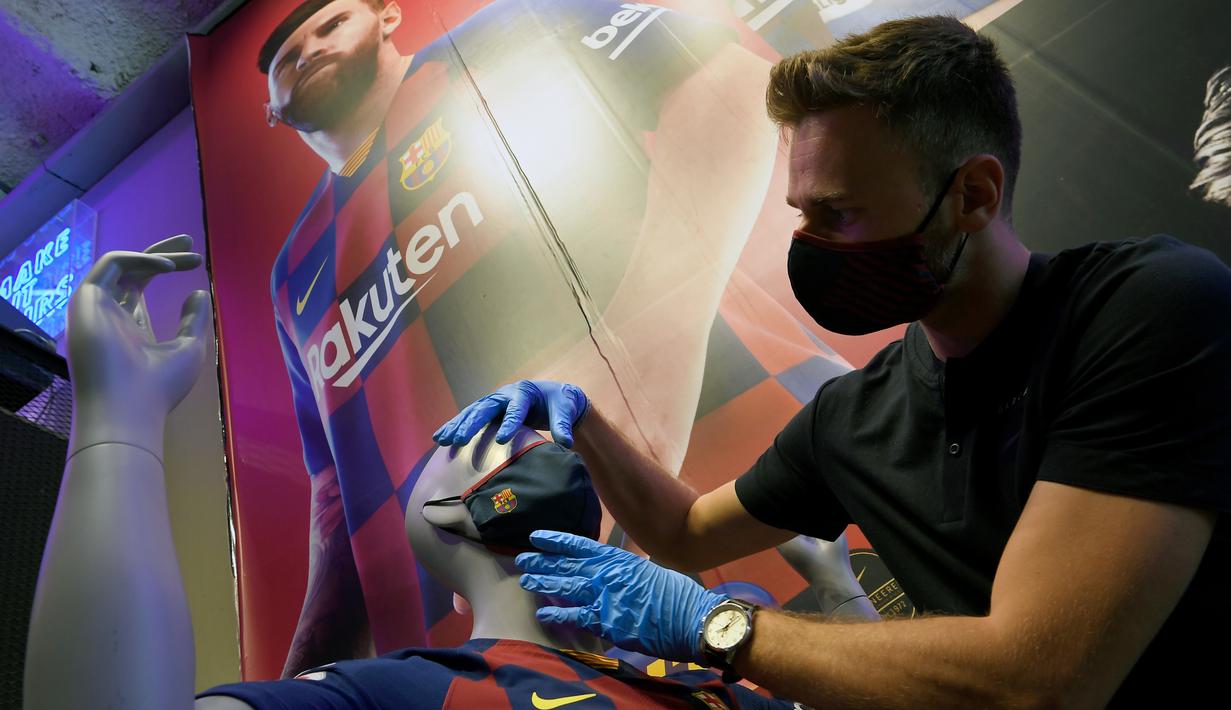 Penjaga toko memasang masker berlogo Barcelona ke Manekin di Toko Asesoris Barcelona, Senin (25/5/2020). Di tengah pandemi virus Corona, Barcelona menjual masker dengan harga 18 euro atau sekitar Rp 291 ribu. (AFP/Lluis Gene)