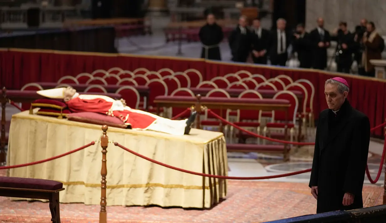 Jenazah mendiang Paus Emeritus Benediktus XVI disemayamkan saat Pastor Georg Gaenswein berdiri di sebelah kanan di Basilika Santo Petrus, Vatikan, Senin (2/1/2023). Benediktus XVI, teolog Jerman yang akan dikenang sebagai paus pertama dalam 600 tahun yang mengundurkan diri, telah meninggal pada 31 Desember 2022 di usia 95 tahun. (AP Photo/Andrew Medichini)