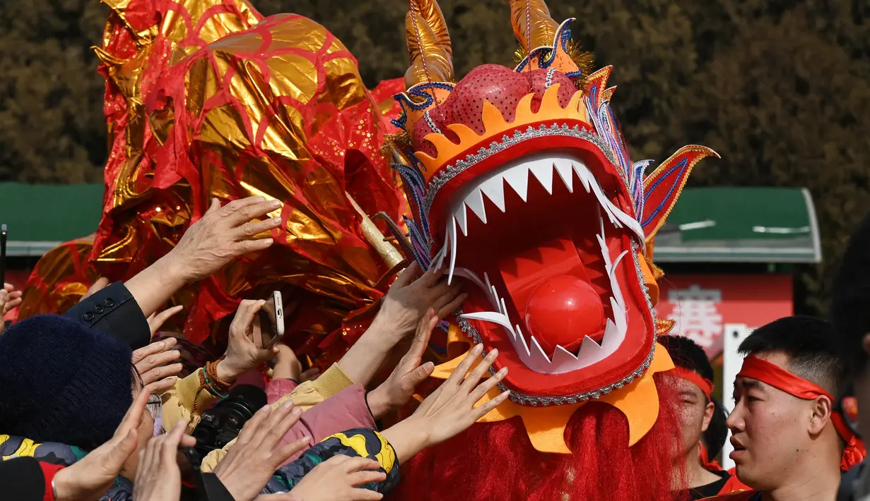 Orang-orang mencoba menyentuh seekor naga saat pertunjukan di sebuah kuil pada hari kedua Tahun Baru Imlek Naga di Beijing pada 11 Februari 2024. (GREG BAKER/AFP)