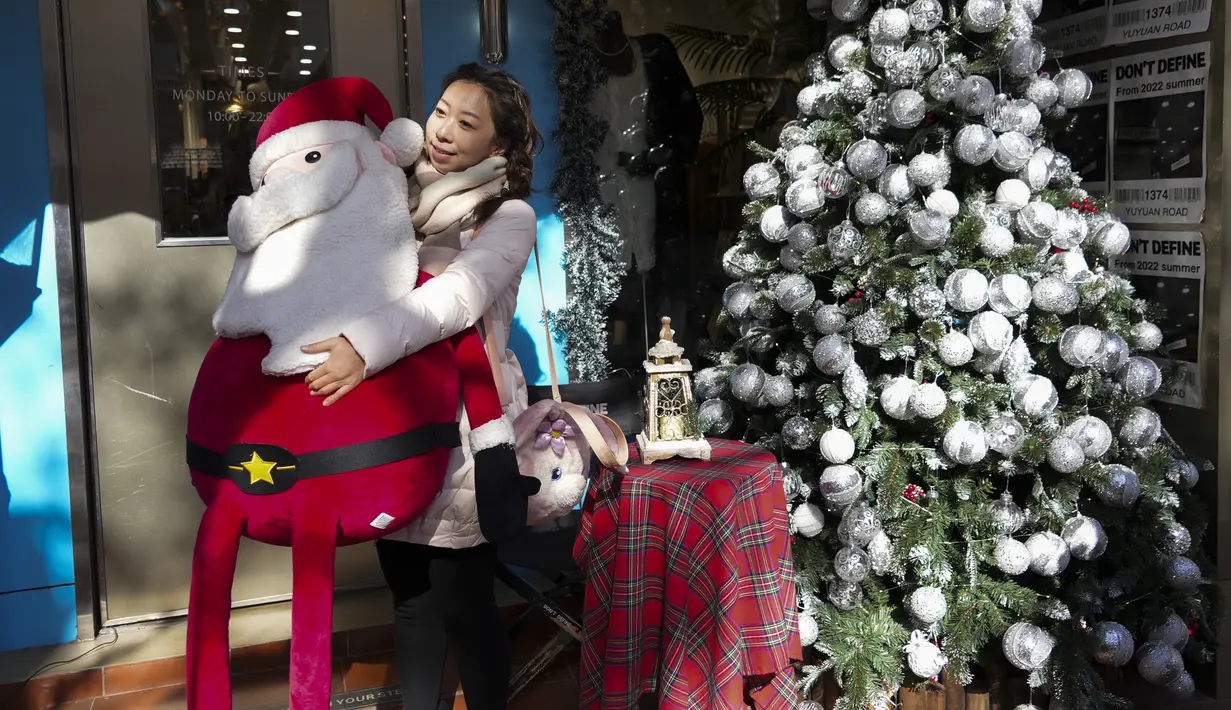 Seorang perempuan memegang boneka Sinterklas saat dia berpose untuk difoto di luar restoran yang didekorasi dengan musim Natal di Shanghai pada 17 Desember 2023. (AP Photo/Wayne Zhang)