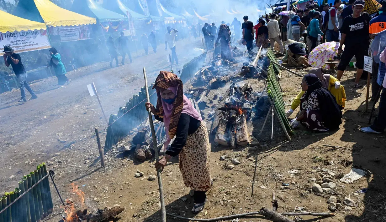 Seorang peserta mengipasi api saat memasak lemang, hidangan nasi ketan tradisional yang dimasukkan ke dalam tabung bambu dan diisi dengan santan yang kemudian diletakkan di atas api terbuka, selama acara memasak massal di Blang Pidie, Kabupaten Aceh Barat Daya, Aceh, pada Sabtu 25 April 2026. (CHAIDEER MAHYUDDIN/AFP)
