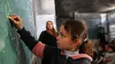 Ada lebih dari 658.000 anak usia sekolah kehilangan akses ke pendidikan formal selama lebih dari dua tahun akademik berturut-turut. Tampak dalam foto, seorang anak pengungsi Palestina menulis di papan tulis selama pelajaran di dalam tenda di Sekolah Mada, kamp pengungsi Jabalia, Jalur Gaza Utara pada 13 April 2026. (Omar AL-QATTAA/AFP)
