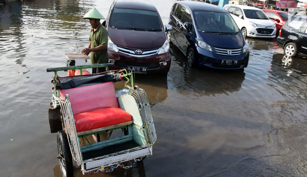 Seorang pria berada di dekat becak di jalan Yos Sudarso Semarang yang terendam banjir di kawasan Pelabuhan Tanjung Emas (24/4). (Liputan6.com/Gholib)