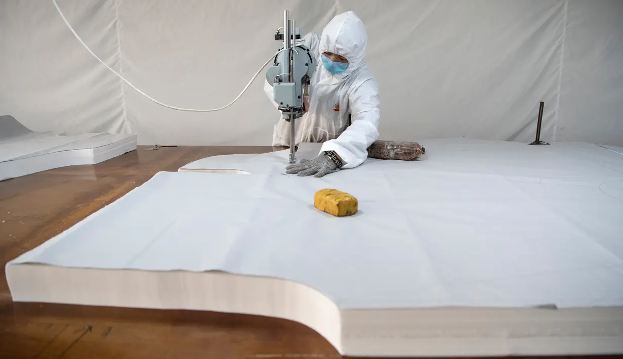 Pekerja memotong bahan untuk digunakan membuat pakaian antivirus di pabrik garmen Zhejiang Ugly Duck Industry, di Wenzhou, 28 Februari 2020. Wabah virus corona di China membuat produsen pakaian itu mulai memproduksi baju hazmat yang banyak diburu orang untuk melindungi dirinya. (NOEL CELIS/AFP)