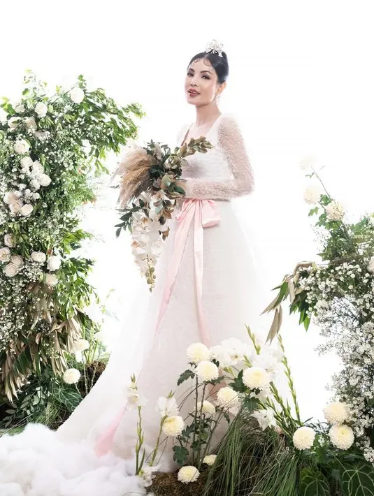 Sambil memegang buket rustic, Nindy tampil dengan gaun panjang putih kerah square dengan lengan panjang lace. Gaun yang dilengkapi pita pink besar sebagai belt dibuat oleh desainer Didi Budiardjo. [@nindyayunda]