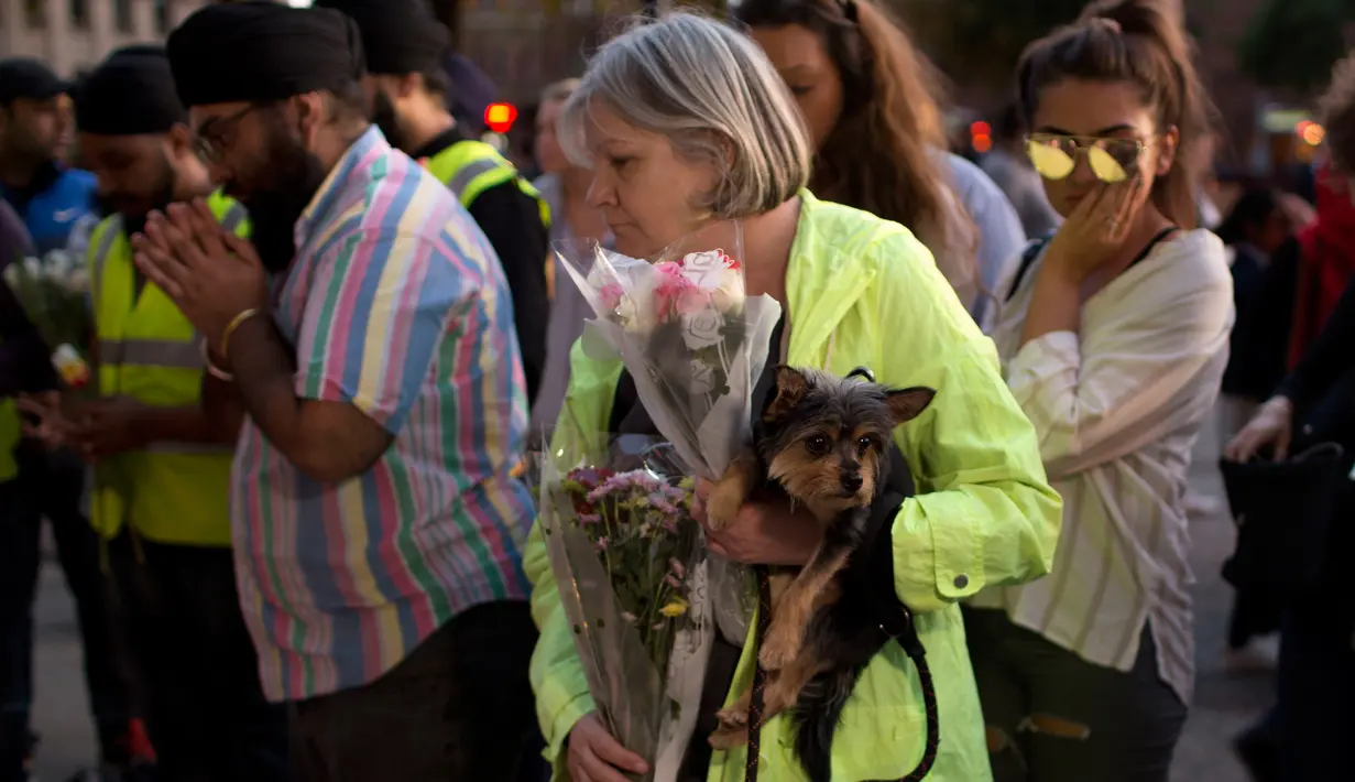 Seorang wanita bersama anjingnya sebelum meletakkan bunga di Albert Square, Manchester, Inggris, (23/5). Kejadian ini menyebabkan 22 orang tewas  dan melukai 119 lainnya. (AP Photo/Emilio Morenatti)