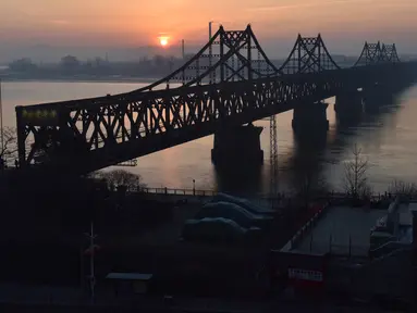 Matahari terbit di belakang Jembatan Persahabatan yang membentang Sungai Yalu antara China dan Korea Utara terlihat dari kota Dandong di provinsi Liaoning timur laut China (22/2). (AFP Photo/Greg Baker)