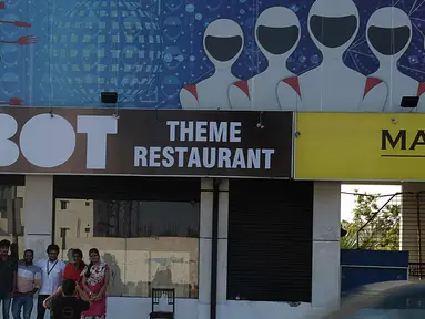 Pengunjung berpose di luar restoran bertema robot di Chennai, India (20/12). Restoran ini merupakan yang pertama di India yang memiliki pelayan robot dengan server otomatis membawa piring dari dapur ke pelanggan. (AFP Photo/Arun Sankar)