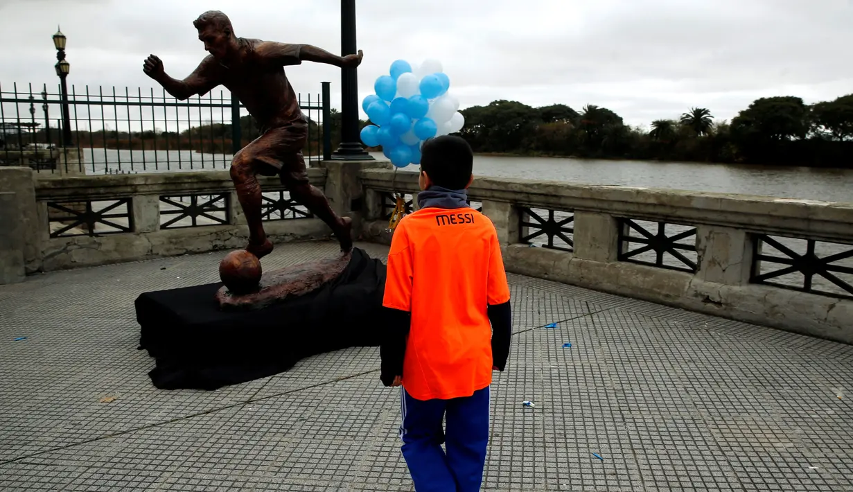 Bocah laki-laki mengenakan jersey Messi mengamati patung perunggu Lionel Messi yang baru diresmikan di Buenos Aires, Argentina, Selasa (28/6). Patung itu guna membujuk Messi membatalkan keputusan pensiun yang sudah diambilnya. (REUTERS/Marcos Brindicci)