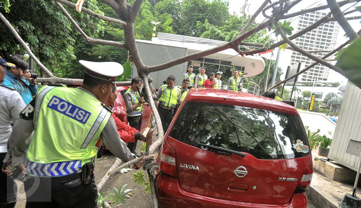 Petugas dibantu warga memindahkan pohon tumbang yang menimpa mobil saat terparkir di sebelah Pos Polisi Bundaran HI, Jakarta, Selasa (15/12). Tak ada korban jiwa akibat tumbangnya pohon yang disebabkan angin kencang tersebut. (Liputan6.com/Faizal Fanani)