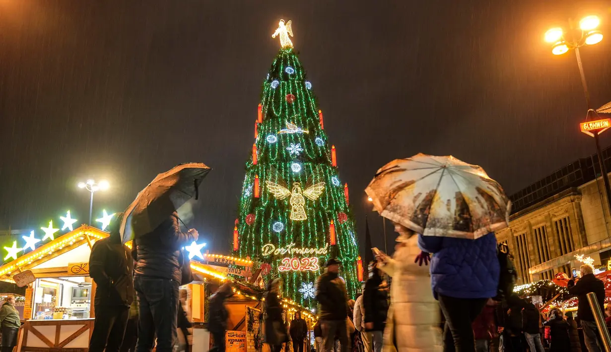 Orang-orang menyaksikan pohon Natal tradisional setinggi 45 meter di tengah hujan lebat di pasar Natal Dortmund, Jerman, Senin, 27 November 2023. (AP Photo/Martin Meissner)