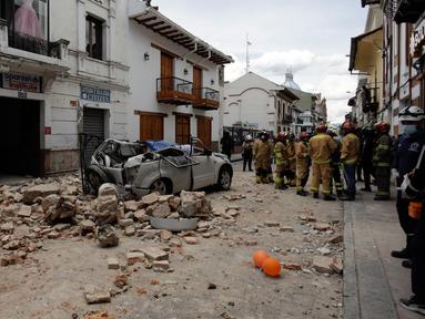 Petugas penyelamat berdiri di samping mobil yang hancur oleh puing-puing setelah gempa bumi di Cuenca, Ekuador, Sabtu (18/3/2023). (AP Photo/Xavier Caivinagua)